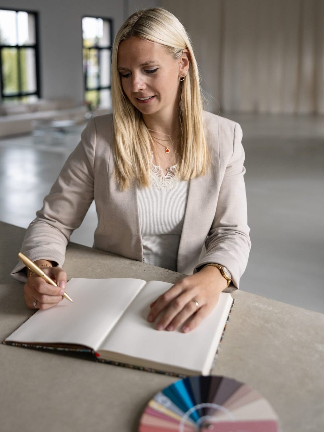 Janin Grundmann schreibt mit einem goldenen Stift in ein Notizbuch, daneben ein Farbfächer