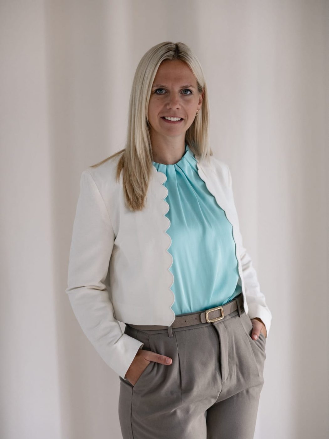 Janin Grundmann im weißen Blazer und türkisfarbener Bluse, die Hände in den Taschen ihrer Stoffhose